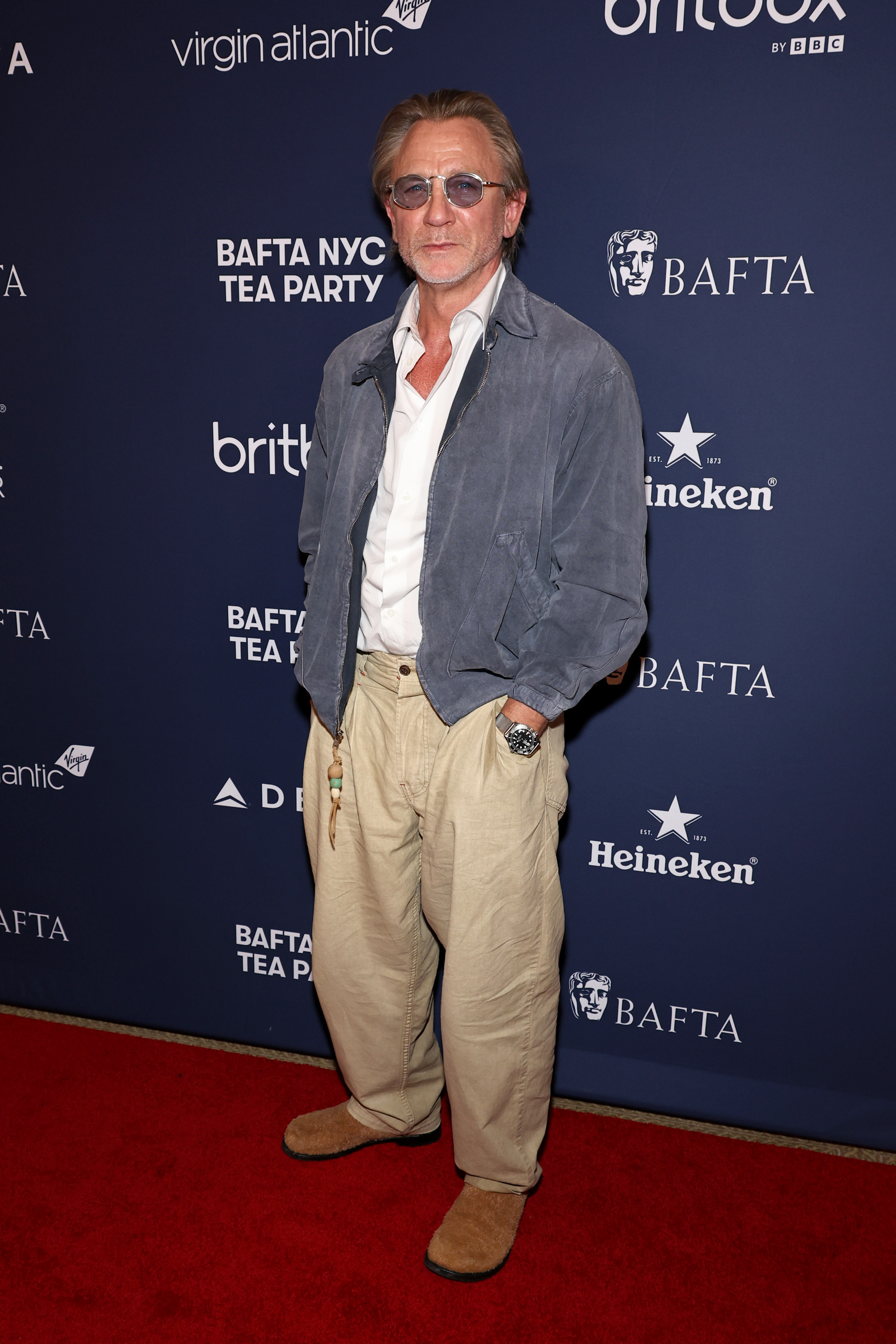 Daniel Craig on the red carpet, wearing a grey jacket, white shirt and loose-fitting beige trousers with tan shoes