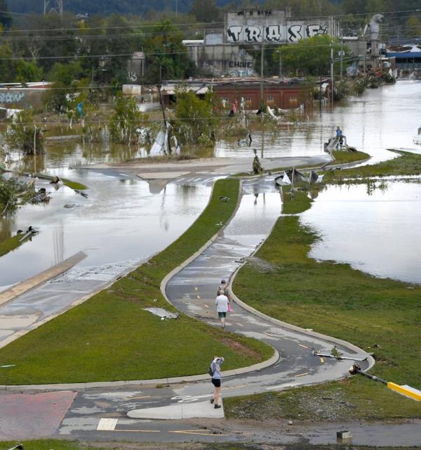 A flooded road in the River Arts District of downtown Asheville, N.C., with people walking on it, after the aftermath of Hurricane Helene.