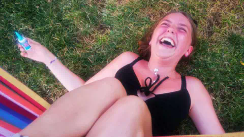 Family Handout Chloe laughs while lying on green grass, she is wearing a black top and silver necklace.
