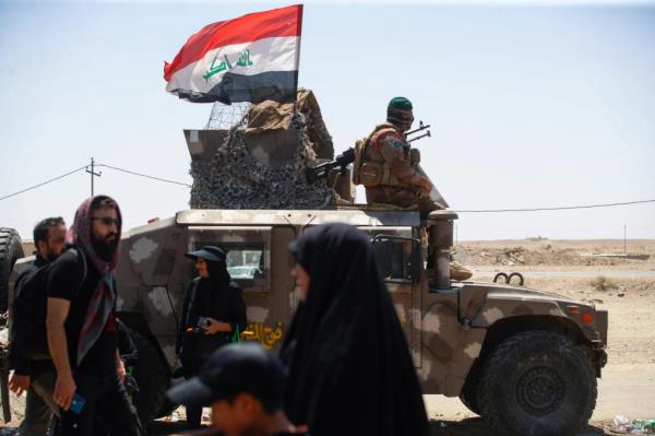 Iraqi security forces stand guard as Shiite pilgrims arriving from Iran walk at the Zurbatiyah border crossing in Iraq's Wasit governorate on August 18, 2024 on their way to the shrine city of Karbala ahead of the Arbaeen commemorations that mark the end of a 40-day mourning period for the seventh century killing of Islam's Prophet Mohamed's grandson Imam Hussein Bin Ali