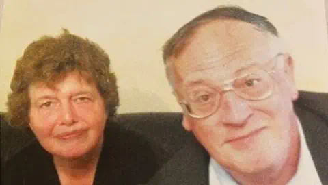 家庭资料:Lois and John McCullough。他们坐在沙发上,对着摄像头微笑。