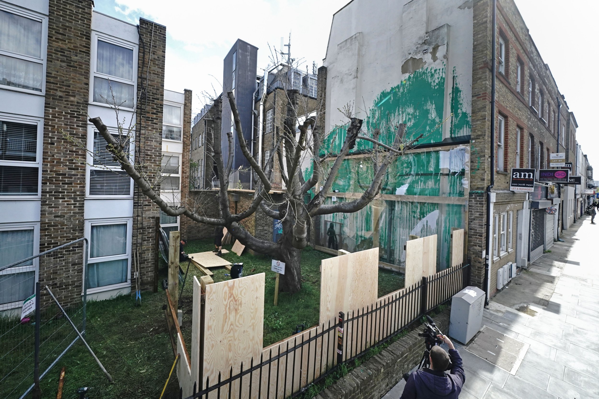 Boarding is put up next to the Banksy artwork on the side of a residential building in Hornsey Road, Finsbury Park, north London, which has been covered in perspex sheeting for protection. The artwork of bright green paint in front of a cut-back tree, creating the impression of being its foliage, with a stencil of a person holding a pressure hose, was defaced with white paint last week. Picture date: Wednesday March 27, 2024. PA Photo. See PA story ARTS Banksy. Photo credit should read: Aaron Chown/PA Wire
