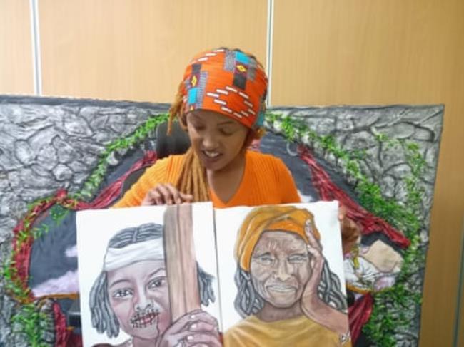 A young African woman holds two paintings as she describes her art