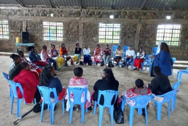 A circle of African women sitting in a hall listening to a woman speaking 