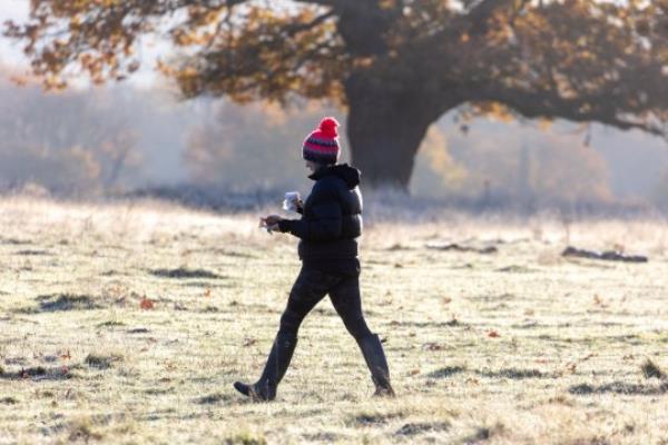 Woman walking in park during frosty week with snow likely, according to the Met Office, as cold weather warning issued