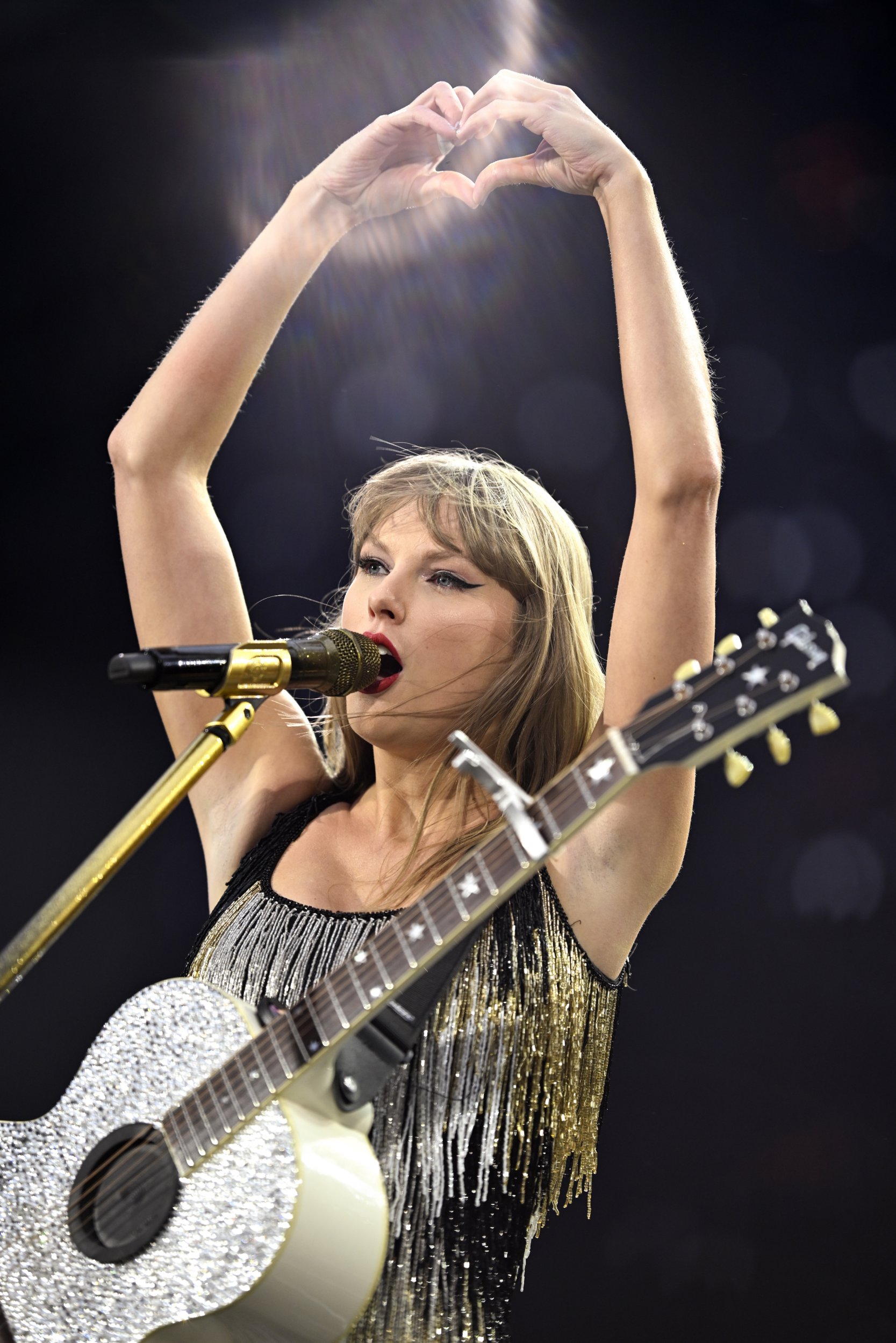 Taylor Swift holds hands above her head in heart shape as she sings during Fearless era of Eras Tour