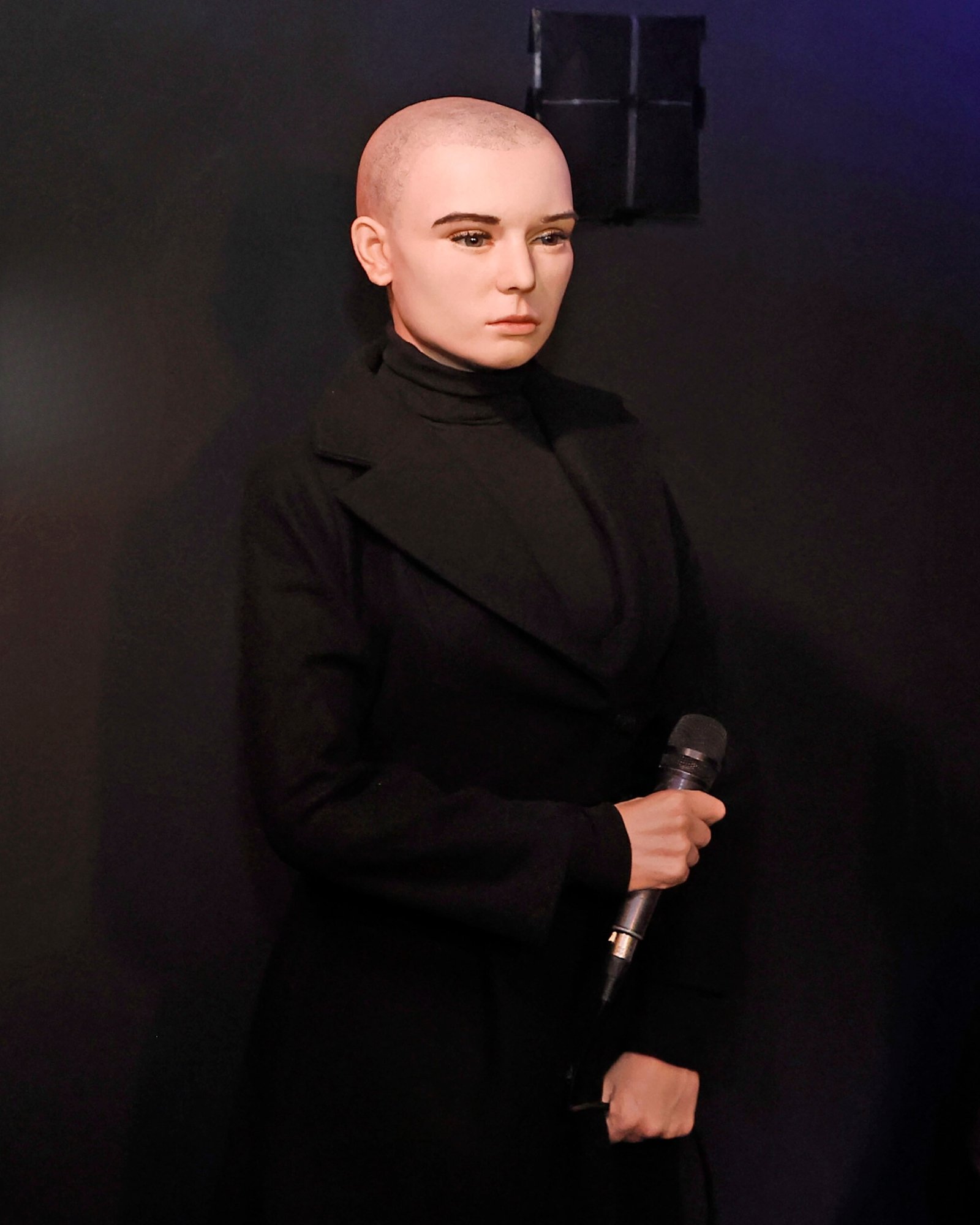 Sinead O'Connor wax figure, dressed in all black and holding a microphone