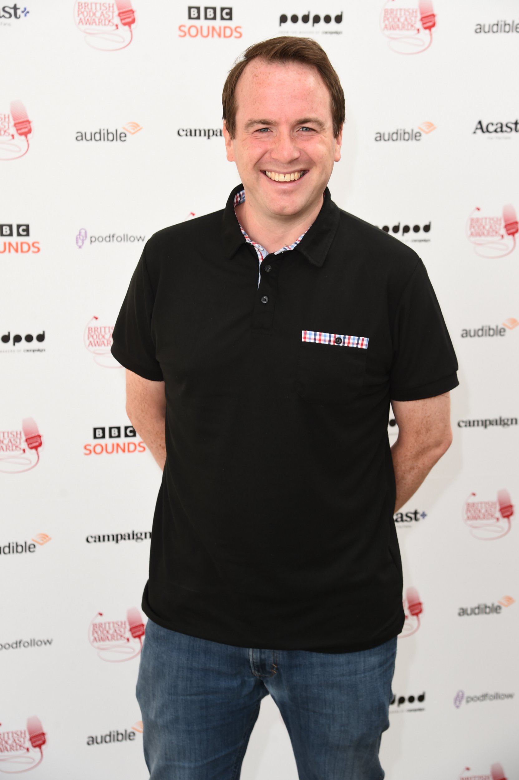 Matt Forde smiling while attending an event. He is wearing a black polo shirt and blue jeans