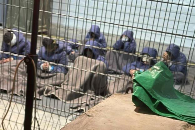 men in blue hoodies sit in a cell