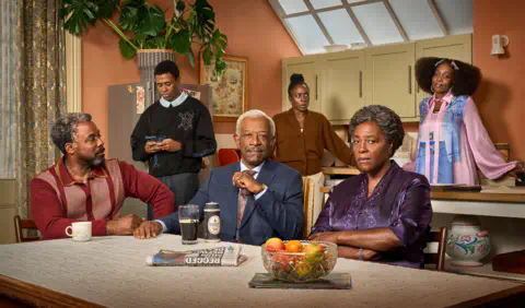 BBC/Fable Pictures/Des Willie Six characters from Mr Loverman in a kitchen with Morris, Barry and Carmel sitting at a table which has a mug, a newspaper, a bowl of fruit and a pint glass of Guinness upon it