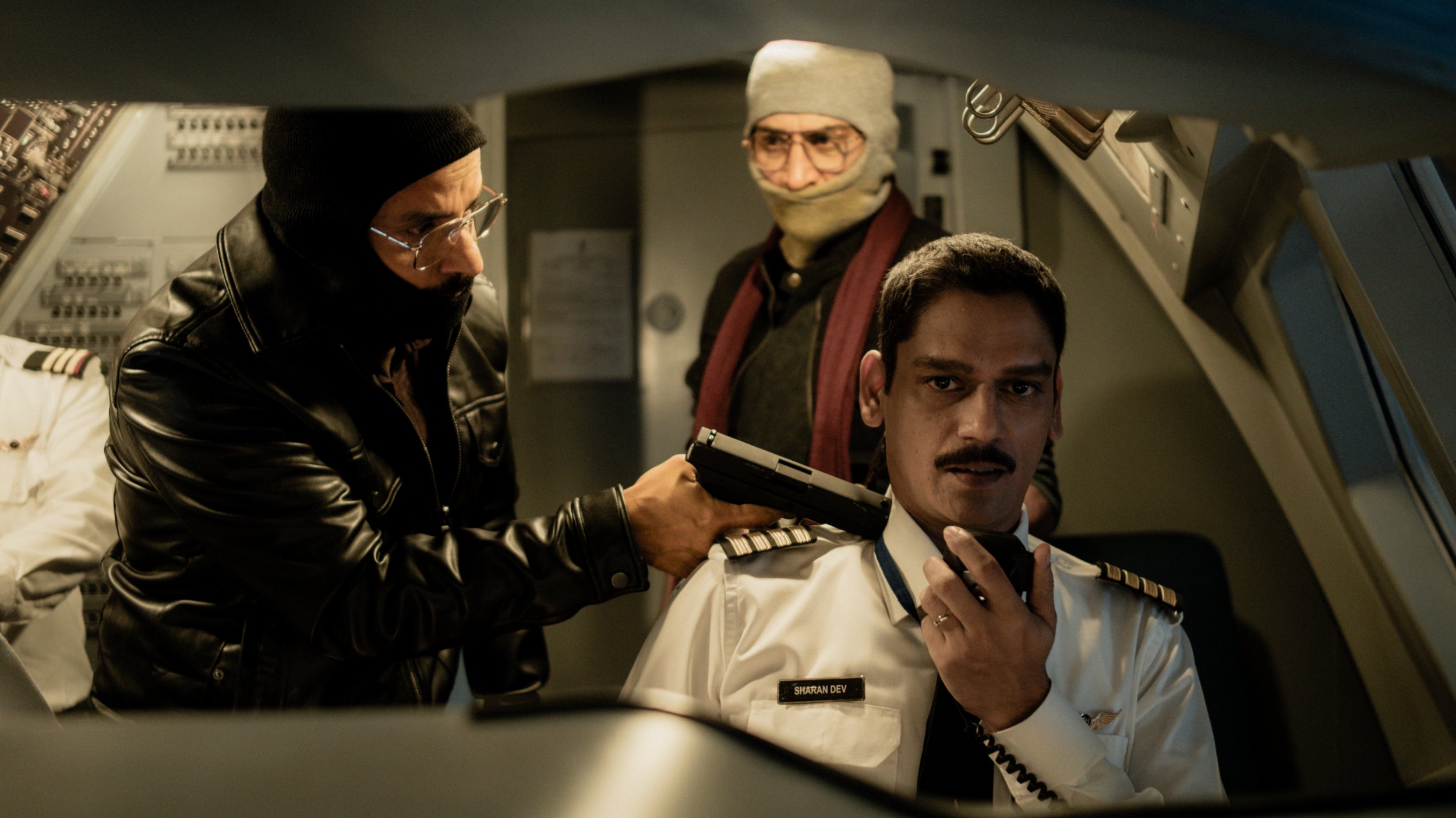 A scene from IC 814: The Kandahar Hijack showing a masked man holding a gun to a pilot.