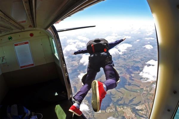 Skydiver seen jumping from plane with clouds and land below him.