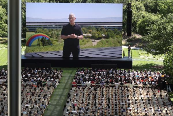 Apple CEO Tim Cook delivering a speech at the Apple Worldwide Developers Conference in Cupertino, California, projected on a large screen with an audience seated.