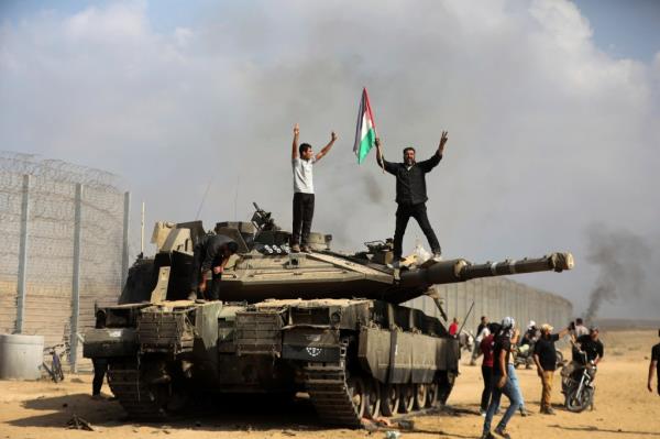 Palestinians wave their national flag and celebrate by a destroyed Israeli tank at the Gaza Strip fence east of Khan Younis.