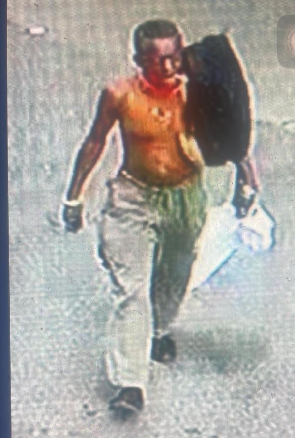 一张监控照片显示该男子在走道上赤裸上身,肩上似乎扛着一个黑色垃圾袋。