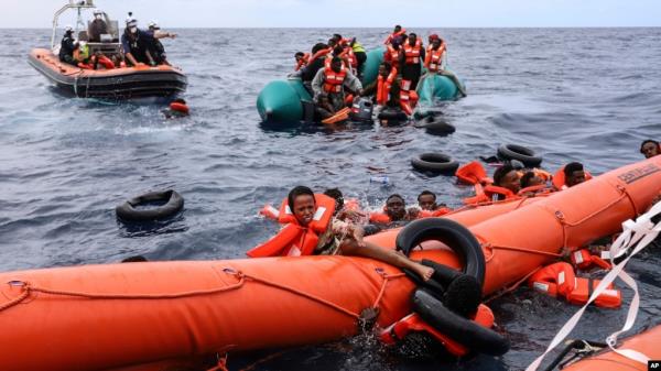 FILE - Migrants aboard a rubber boat end up in the water while others cling on to a centifloat before being rescued by a team of the Sea Watch-3, around 35 miles away from Libya, Oct. 18, 2021. 
