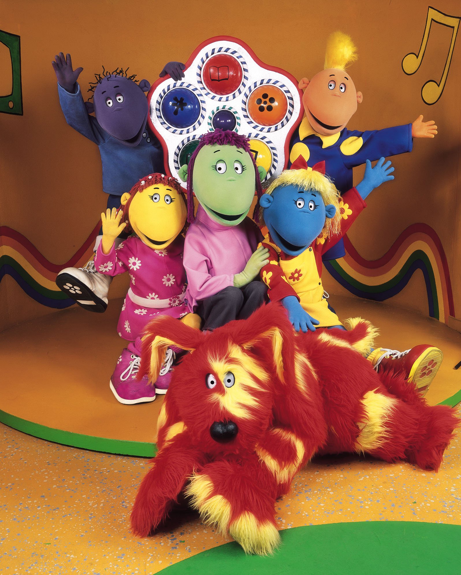Tweenies star Milo, Fizz, Judy, Bella, Jake and Doddles posing in a yellow room painted with musical notes