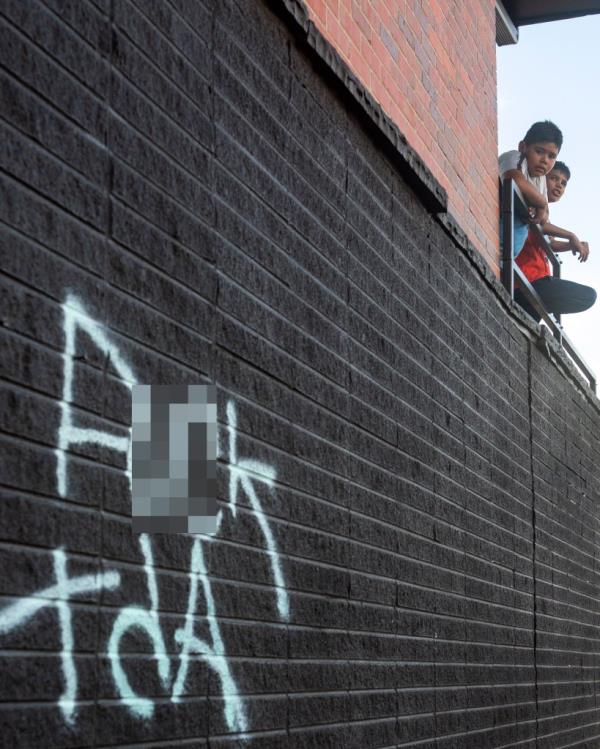 Two boys stand on an apartment balcony in Aurora, Colorado, where anti TdA graffiti is painted.