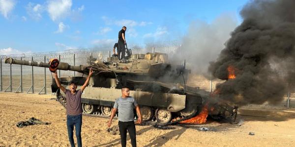 Palestinians react as an Israeli military vehicle burns after it was hit by Palestinian gunmen who infiltrated areas of southern Israel, at the Israeli side of Israel-Gaza border.