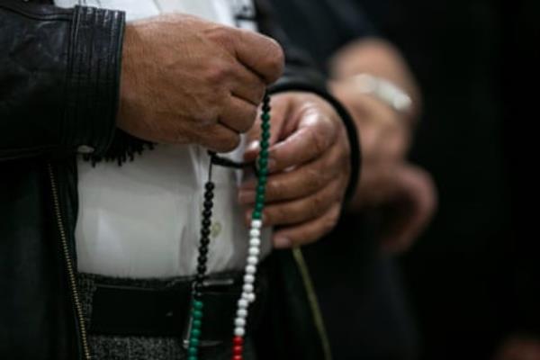 a closeup of hands holding green, white and red prayer beads