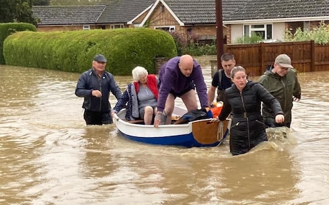 Simon O'Brien (left) using his homemade boat, which he built for his grandchildren, to rescue elderly residents from their home in the village of Debenham, Suffolk
