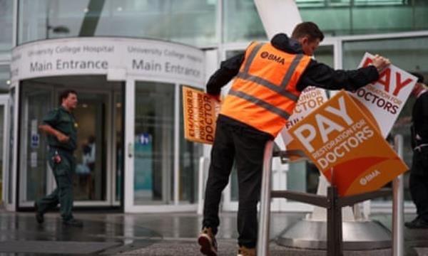 Man wearing BMA hi vis arranging doctor's strike placards outside University College Hospital, London