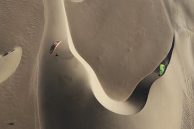 Two paramotorists fly over crescent dunes 