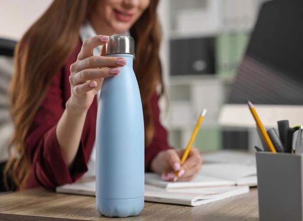 A woman at her desk using a blue water bottle with a metal cap