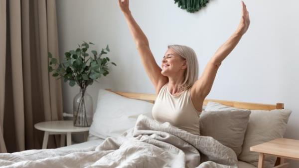 A mature woman looking happy and stretching in bed.