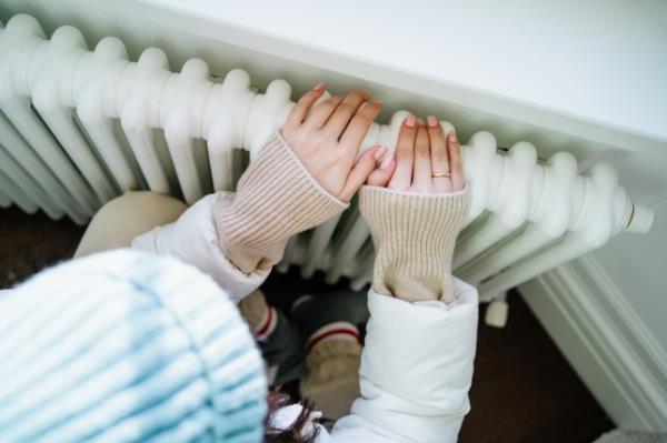 Close up woman in hat getting warm with hands on radiator indoors