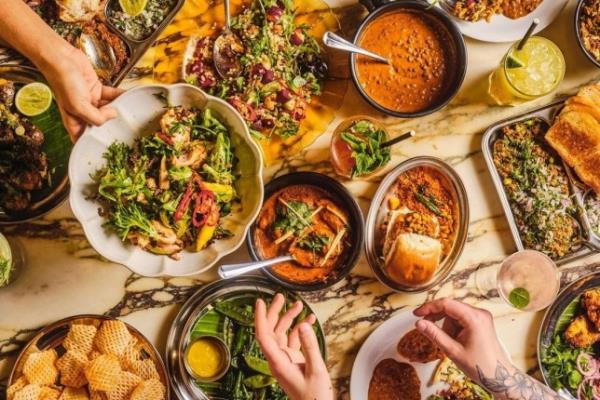A spread of Dishoom's new menu items on a table, with hands passing dishes around