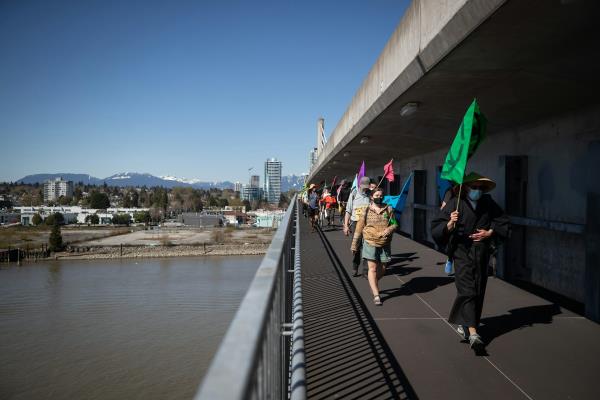 People with banners walking on a bridge over a river.