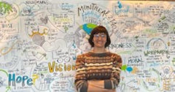A woman in front of a poster featuring words like 'worldbuilding' and 'hope.'