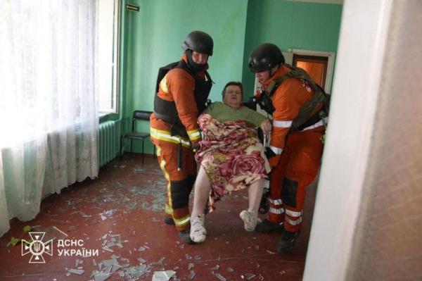 Two rescuers carryong an elderly woman after Russia bombed a care home in Sumy. There is glass all over the floor