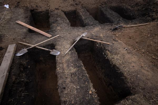 Shovels lay across freshly dug graves for victims of a Russian missile attack in the village of Hroza