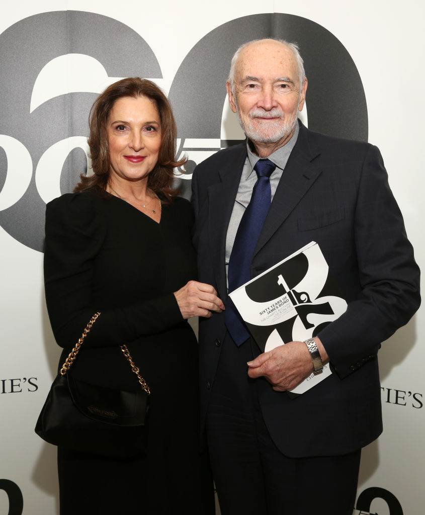 Barbara Broccoli in a black skirt suit and Michael G. Wilson in a blue suit and tie pose arm in arm at a Bond-themed Christies auction