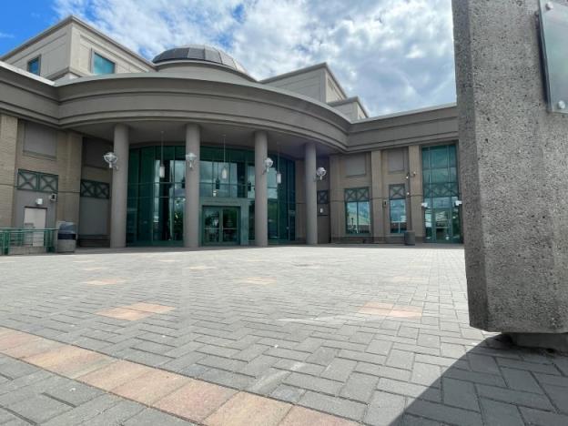 A shot from the ground looks up at the courthouse, an imposing grey building with cement pillars, a cupola, and a large plaza of paving stones.