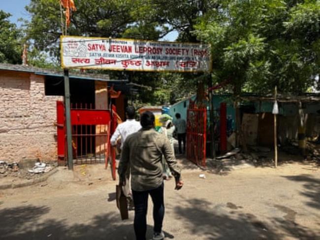 A few Indians seen from behind going into a compound with the name of the society above the gate