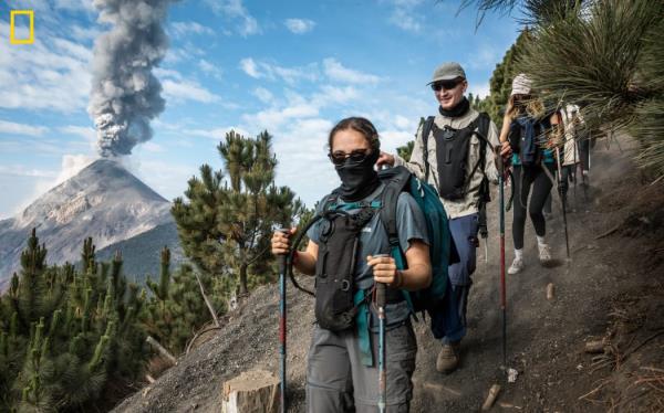 在危地马拉安提瓜，Volcán de Fuego火山在远处喷发，徒步旅行者正在攀登