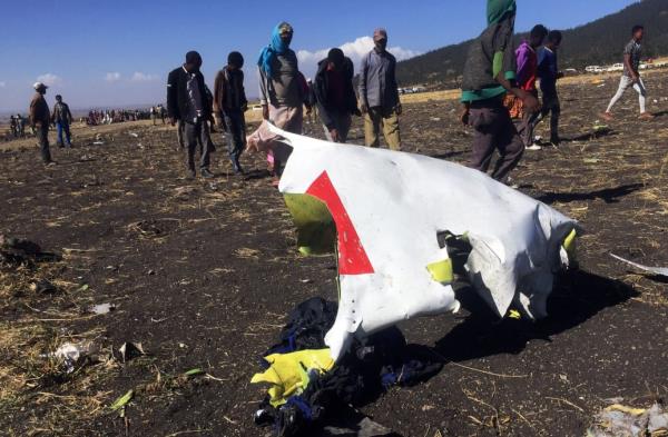People walk past a part of the wreckage at the scene of the Ethiopian Airlines Flight ET 302 plane crash