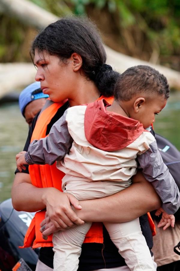 A migrant carrying a toddler boards a boat with other migrants heading north, in Bajo Chiquito in the Darien province of Panama, Thursday, Oct. 5, 2023