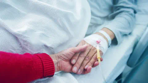 Getty Images A hand holding the hand of a person lying in a hospital bed. 