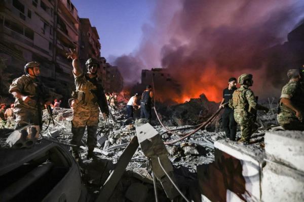 Lebanese army soldiers stand on top of the rubble of a leveled buildings as other fight the flames on Sept. 27, 2024.