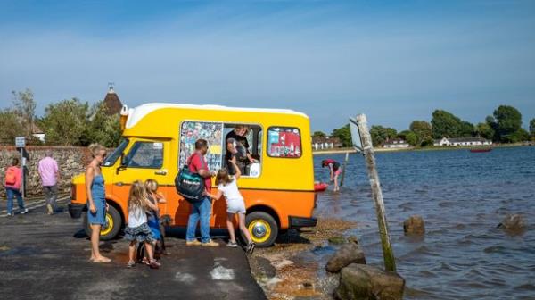 A young girl reaches for an ice cream from a man selling from an ice cream van in Bosham, West Sussex