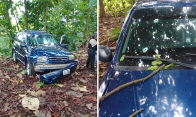 A blue car, with a smashed front bumper, in some woodland. 