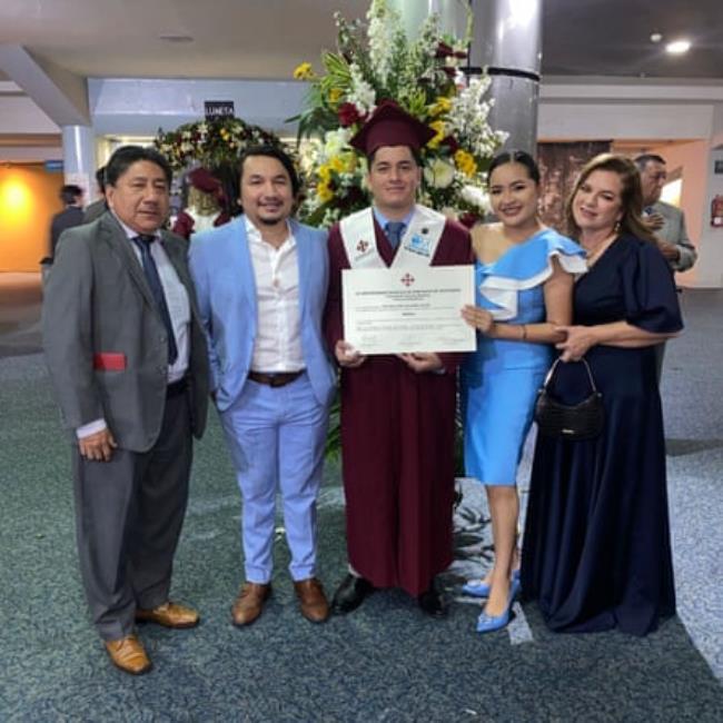 A man in graduation robes stands with his family