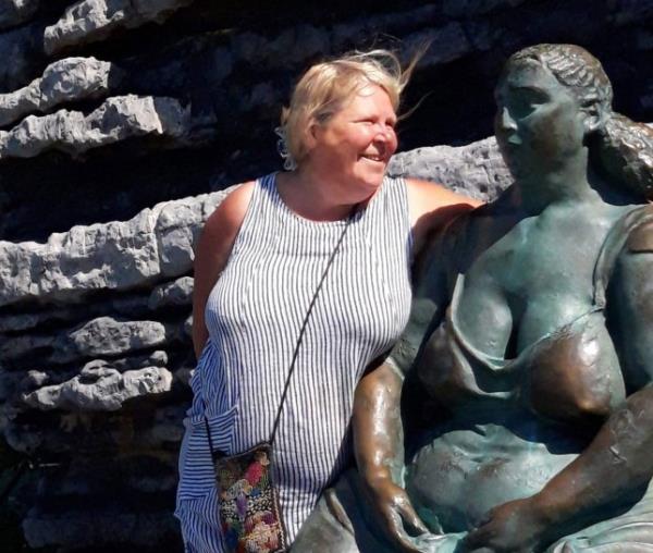 Gill Allbutt, who embraced naturism after splitting from her husband of 40 years, is pictured wearing a striped dress next to a statue of a woman wearing a low-cut top