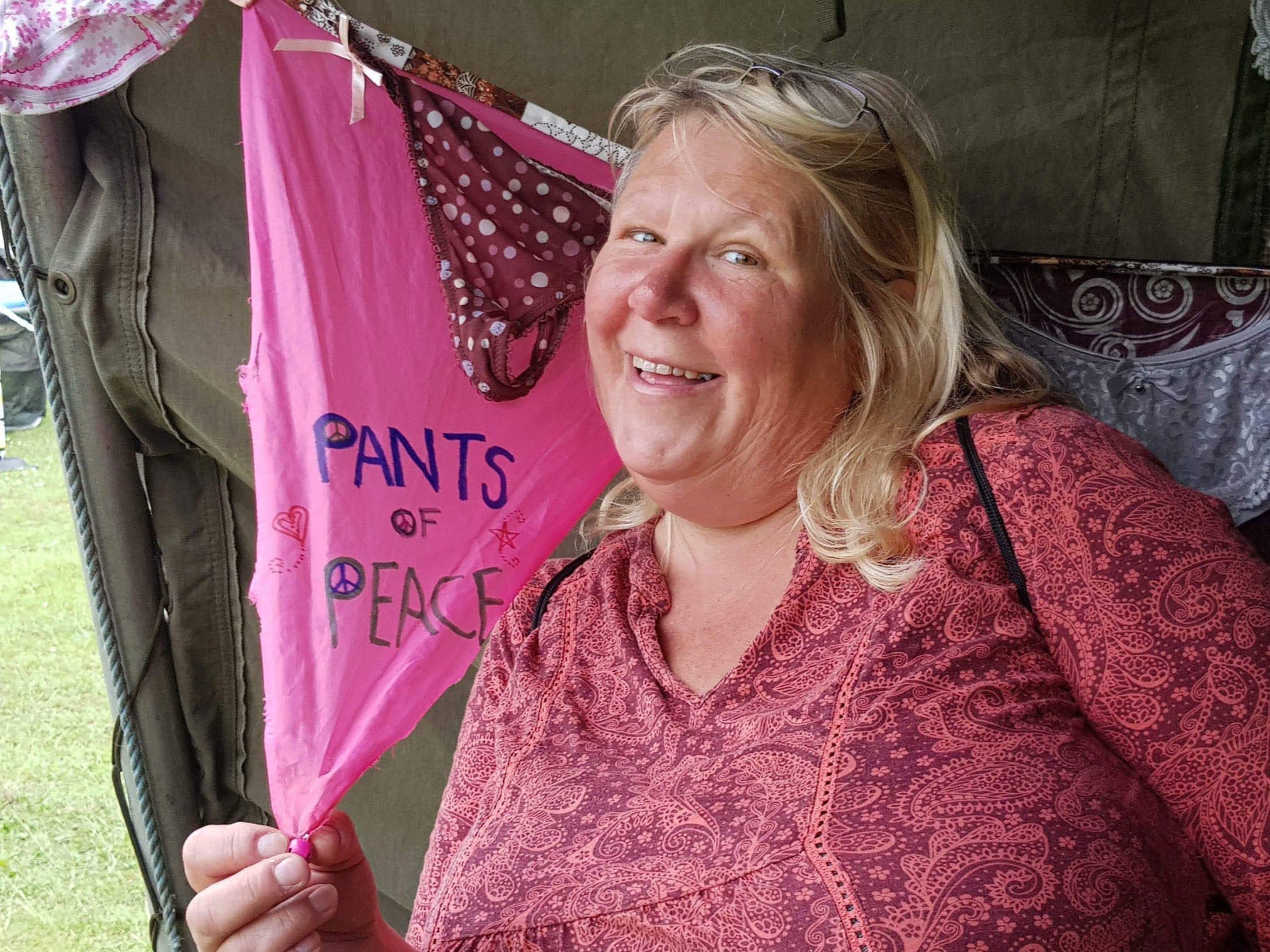Gill Allbutt, who embraced naturism after splitting from her husband of 40 years, is pictured wearing a pink patterned top next to bunting made out of underwear with the words 'pants of peace' over the front