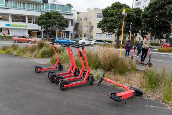 Shared e-scooters lined up on the edge of a road with people riding some behind them