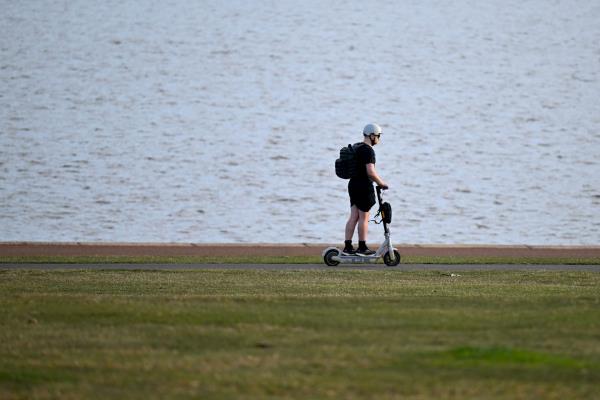 A man rides an e-scooter along a lakeside path